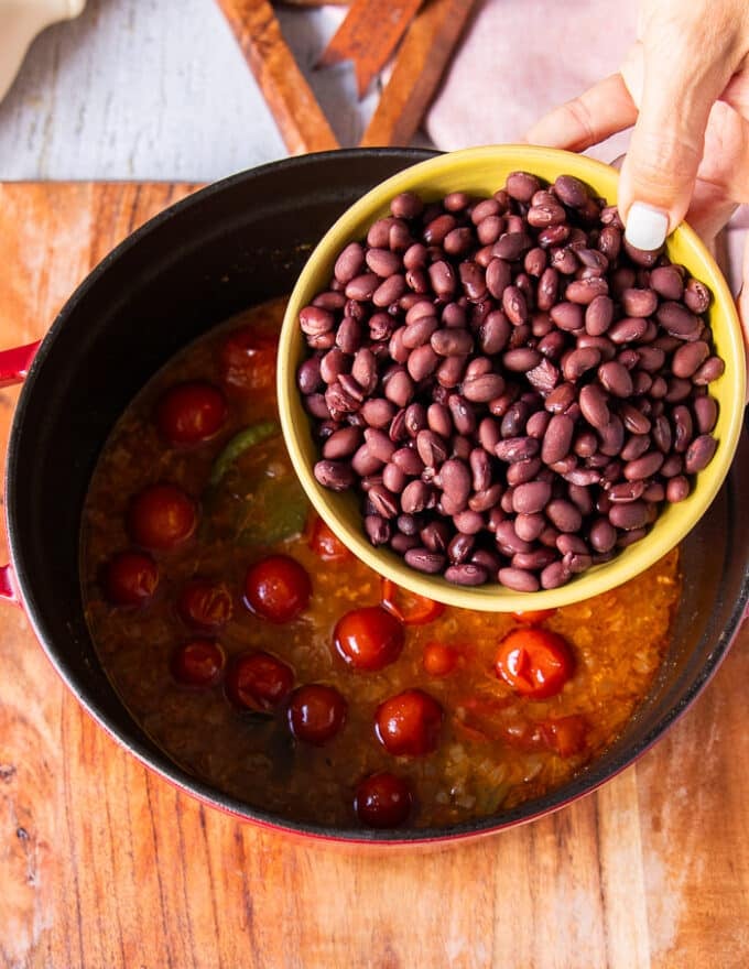 A hand holding in the bowl of black beans and adding it into the soup pot