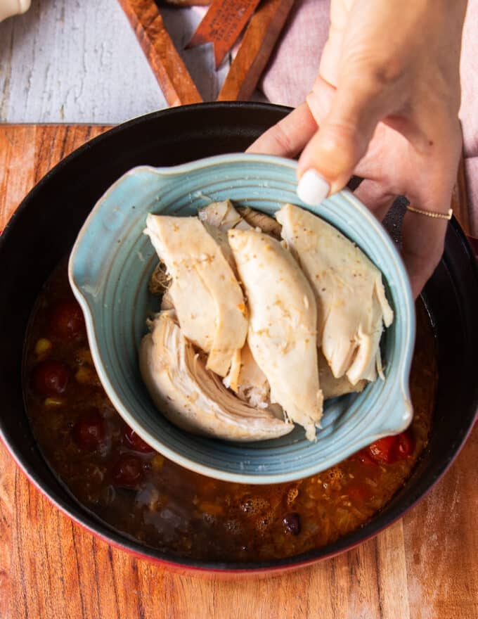 A hand holding in the cooked chicken and ready to add it into the soup