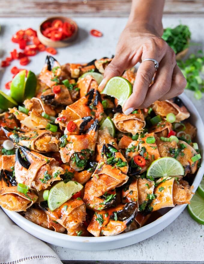 A hand squirting lime juice over a plate of cooked crab claws