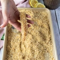 A hand holding a piece of fish coated in toasted breadcrumbs showing how it should be coated