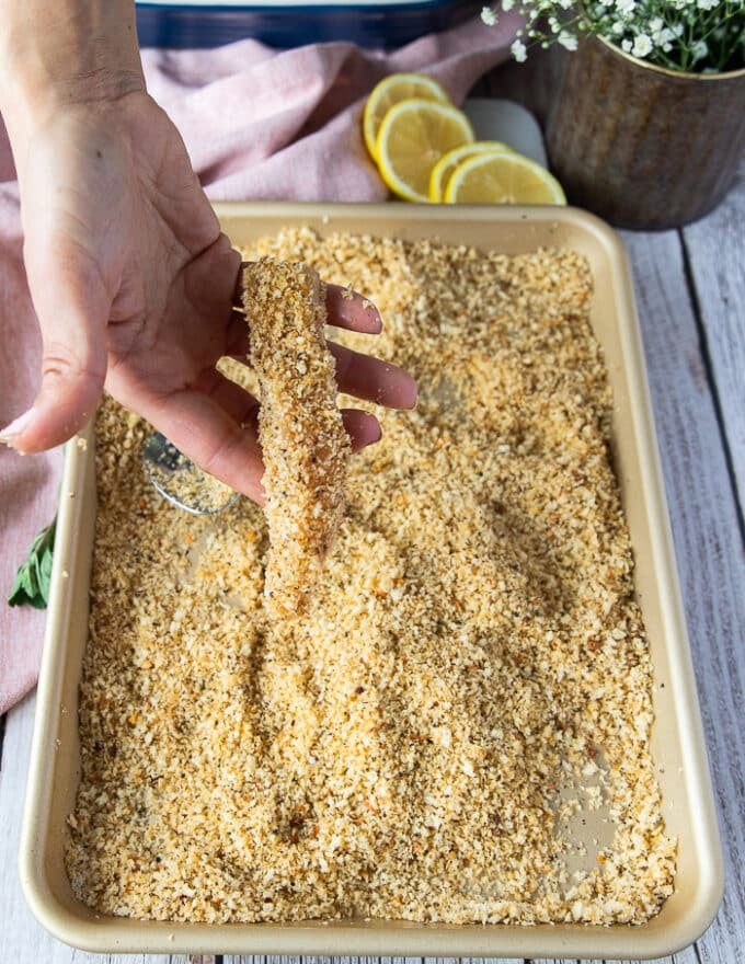 A hand holding a piece of fish coated in toasted breadcrumbs showing how it should be coated