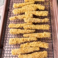 The coated fish fingers in breadcrumbs arranged on a cooling rack on the baking sheet ready to bake