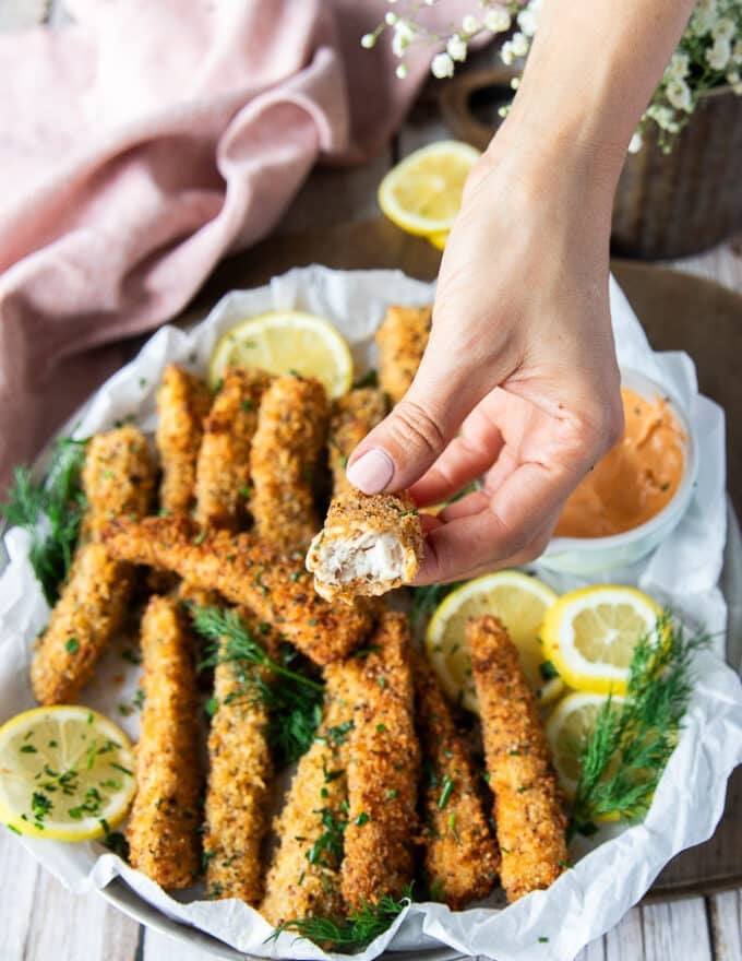 A hand holding a bitten piece of fish stick showing the texture on the inside. succulent cooked fish fingers on the inside with a crisp outside