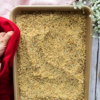 A hand holding a sheet pan of the toasted panko bread crumbs mixture
