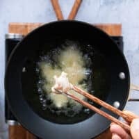A hand holding chopsticks and adding the coated chicken one by one into the hot oil