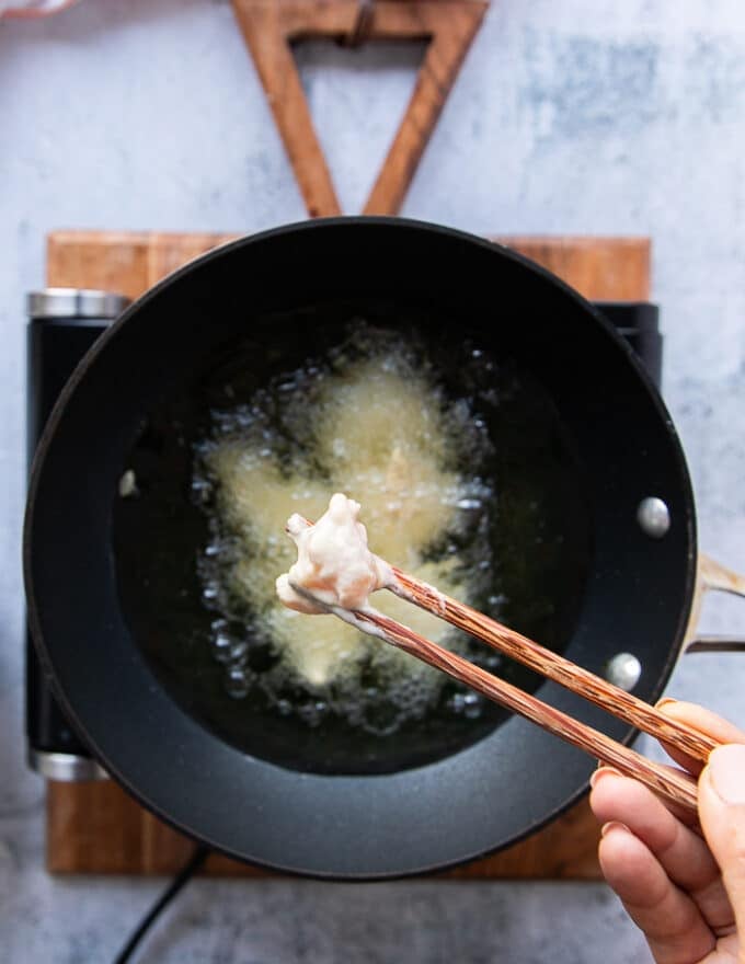 A hand holding chopsticks and adding the coated chicken one by one into the hot oil 