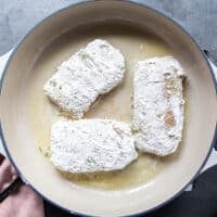 The cod fish coated in flour placed in a non stick skillets with butter
