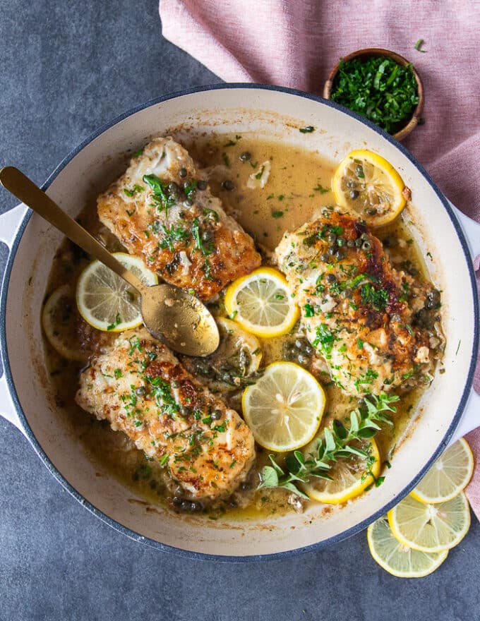 The pan seared cod is ready. The fish is cooked in the lemon butter sauce and garnished with lemon sliced and more fresh oregano in a large skillet 