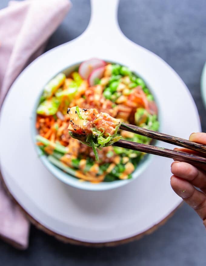 A hand holding a chopsticks and lifting a chunk of the poke bowl to show the seasoned and drizzled bowl