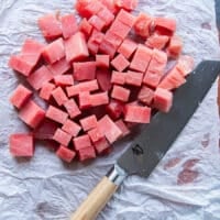 The ahi tuna chopped up into 1 inch dice on a cutting board with a knife nearby