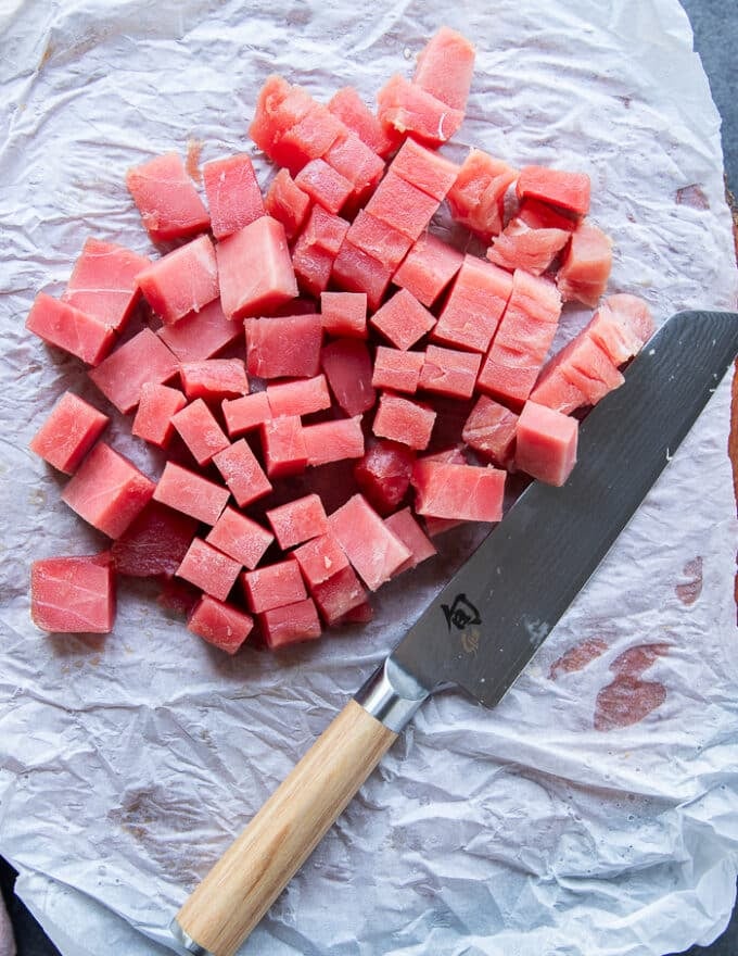 The ahi tuna chopped up into 1 inch dice on a cutting board with a knife nearby