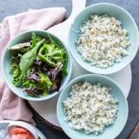 Three bowls on a table, some bowls have sushi rice as a base, some bowls have salad as a base ready to assemble the bowls