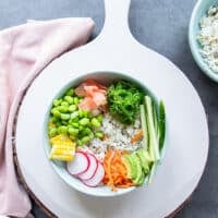 The veggies are layered around the bowl with sushi rice including some edamame, cucumbers, seaweed, carrots, pickled ginger, corn, radishes