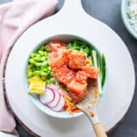 A hand holding a spatula and scooping in the diced chunks of seasoned tuna in to the center of the poke bowls