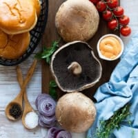 ingredients for the portobello mushroom burger including portobello mushrooms, seasoning, olive oil, spicy mayo, burger buns, cheddar cheese, onions, lettuce, tomatoes