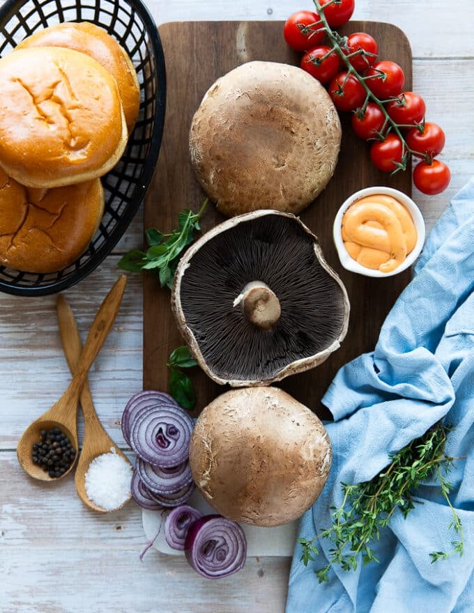 ingredients for the portobello mushroom burger including portobello mushrooms, seasoning, olive oil, spicy mayo, burger buns, cheddar cheese, onions, lettuce, tomatoes 