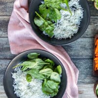 Two bowls on a wooden board with a base of rice and optional some spinach on the side.