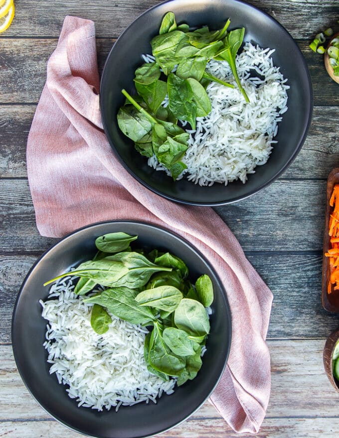 Two bowls on a wooden board with a base of rice and optional some spinach on the side.