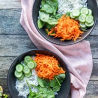Shredded carrots, sliced cucumbers and avocados are arranged over the rice.