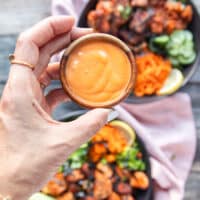 A hand holding a bowl of homemade spicy mayo ready to drizzle of the salmon bowls