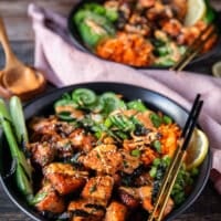 close up of aa salmon bowl showing the salmon loaded over rice, some seaweed, some carrots, cucumbers, avocado all arranged in the bowl and drizzled with spicy mayo