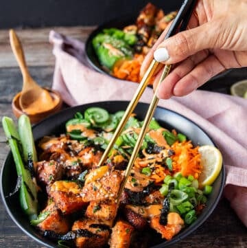 A hand using two chopsticks to grab a bite of the salmon bowls