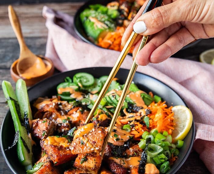 A hand using two chopsticks to grab a bite of the salmon bowls