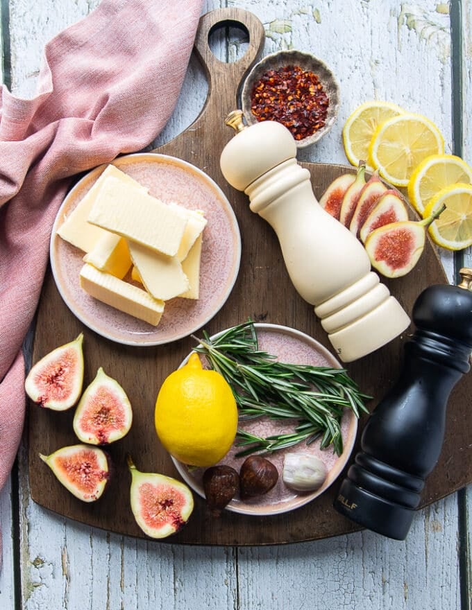 Ingredients to make the lamb loin chops recipe including the lamb loins, the butter, some lemon, dried figs, fresh rosemary, salt, pepper and onion flakes 