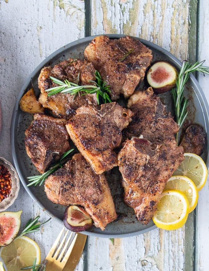 A plate with the cooked lamb loin chops surrounded by fresh rosemary 