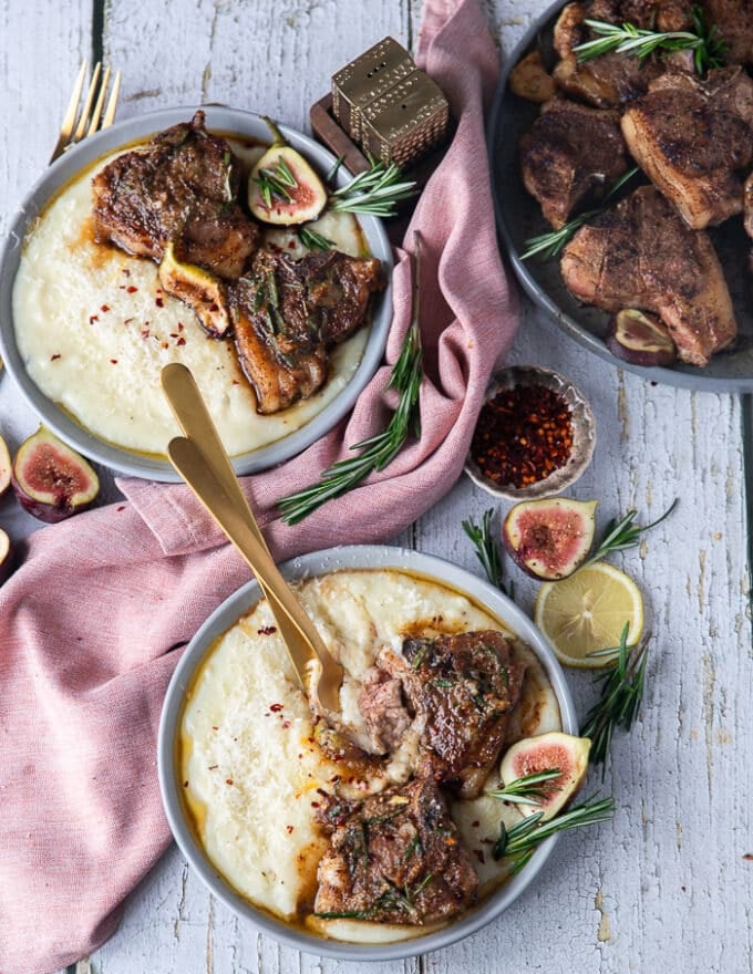 Two plates with lamb loin chops served over mashed potatoes and the rosemary butter on the side , some cutlery in one plate is showing how to eat the lamb loin chops 