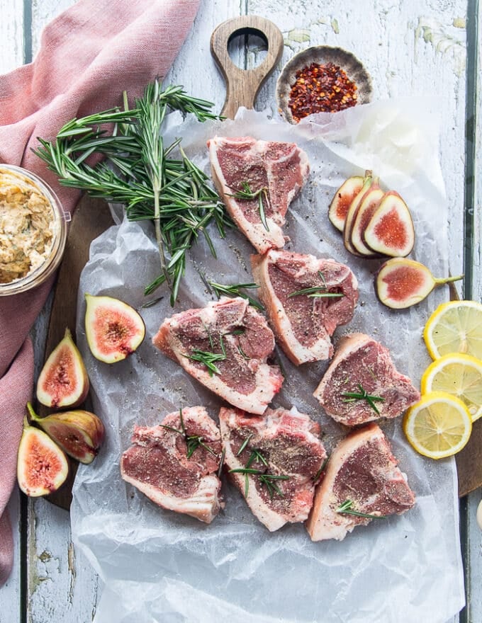 Lamb loin chops on a parchment paper seasoned on both sides with salt, pepper, onion flakes and fresh rosemary 