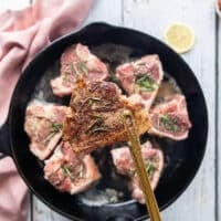 One hand flipping the lamb loin chops in the pan to show the golden crust