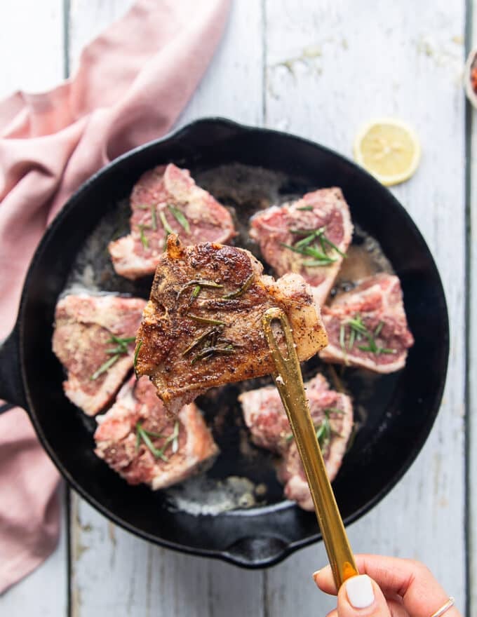 One hand flipping the lamb loin chops in the pan to show the golden crust 