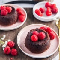 two plates of molten chocolate cake on small plates topped with fresh raspberries and ice cream optional on a separate bowl