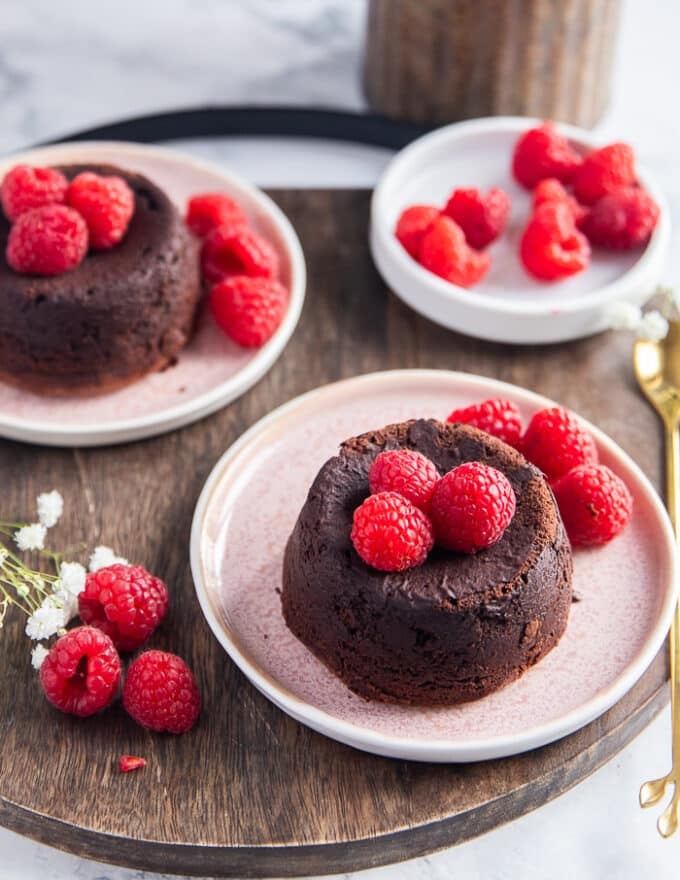 two plates of molten chocolate cake on small plates topped with fresh raspberries and ice cream optional on a separate bowl