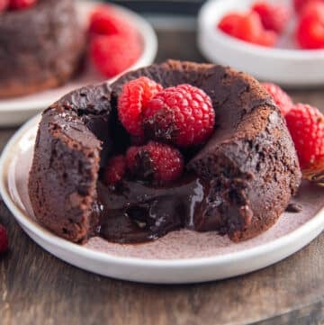 A molten lava cake broken in the middle showing the oozing chocolate center and some raspberries on the top