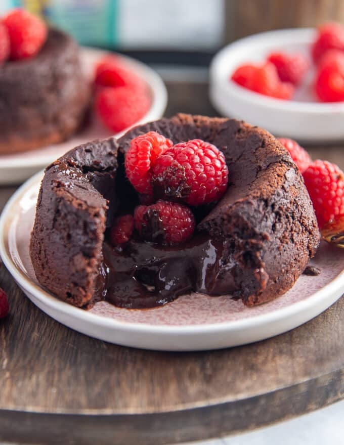 A molten lava cake broken in the middle showing the oozing chocolate center and some raspberries on the top