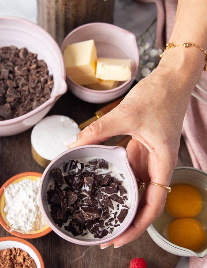 A hand holding the bowl of cream and chocolate chunks melted to form the truffle center of the lava cake recipe