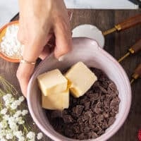 A hand holding a bowl with chopped chocolate bark and unsalted butter ready to melt them together.
