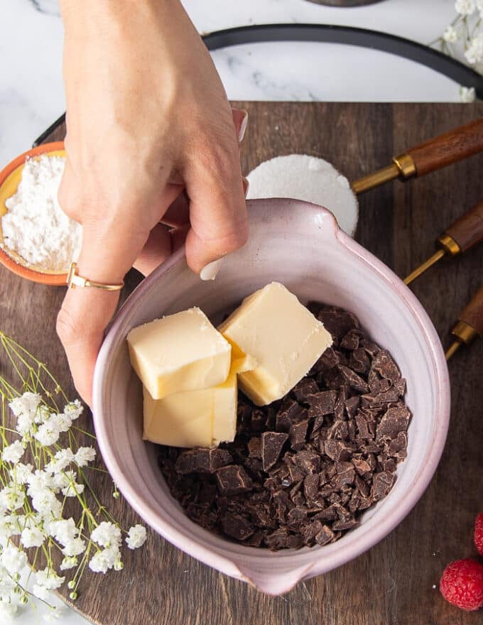 A hand holding a bowl with chopped chocolate bark and unsalted butter ready to melt them together.