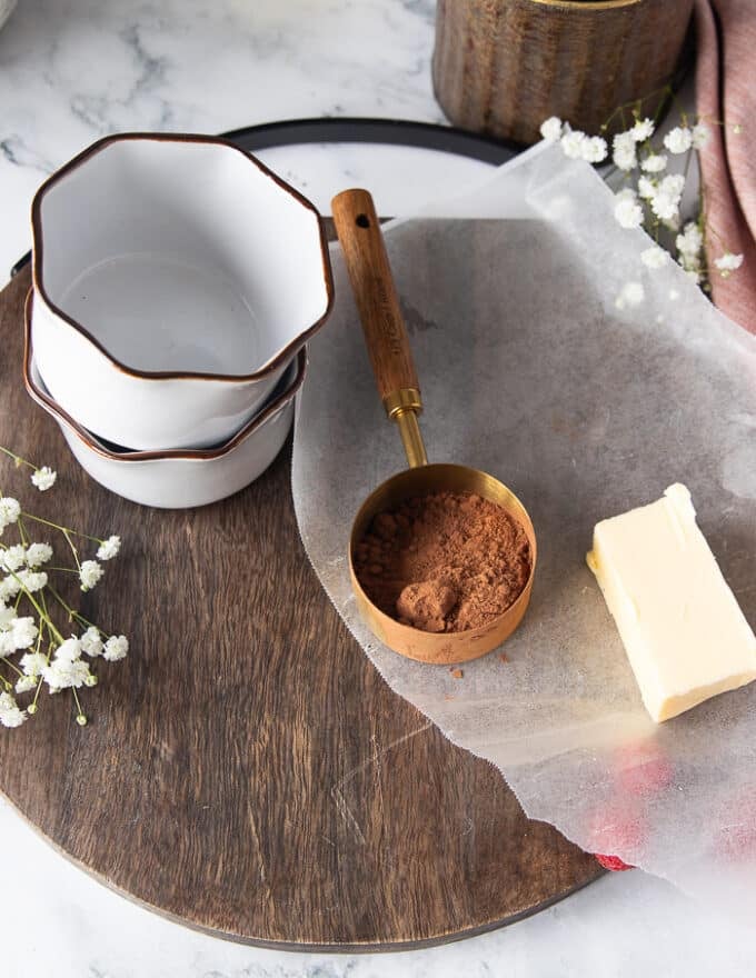 A set of two ramekins, some room temperature butter and a measuring cup of cocoa powder