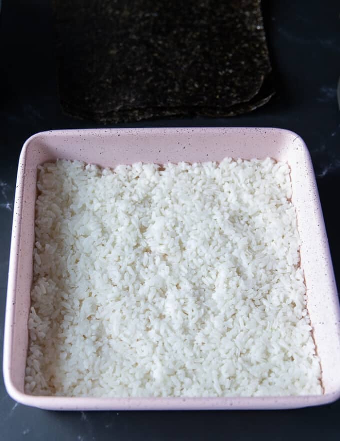 Sushi rice is flattened and spread into a 9 inch square baking pan