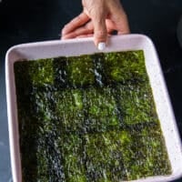 The seaweed sheet is placed evenly over the sushi rice in the baking pan and pressed down