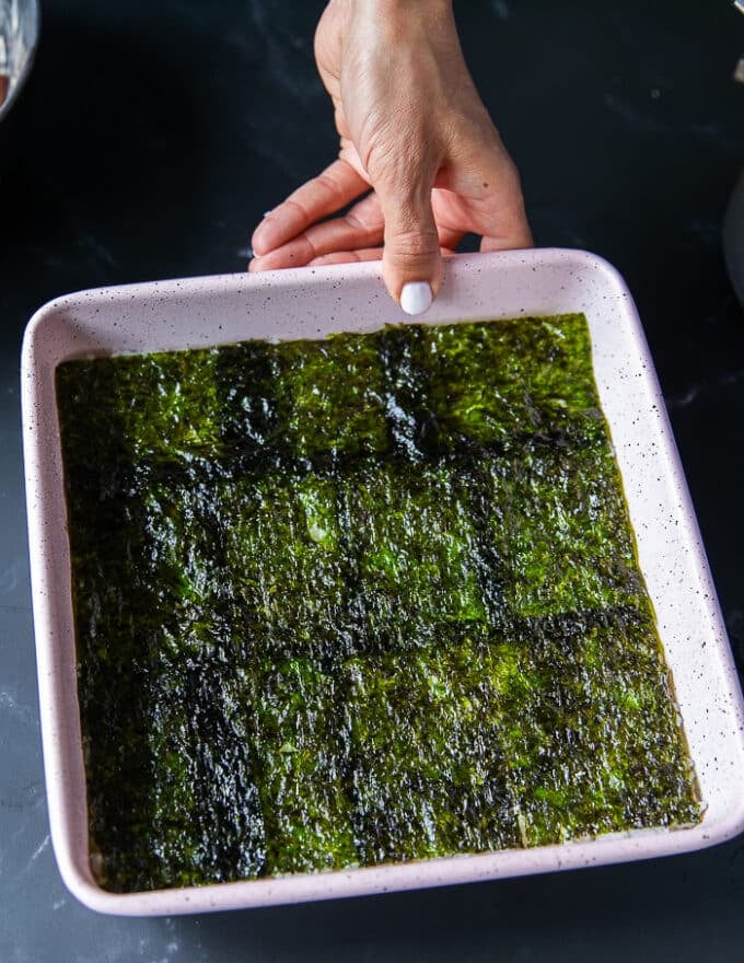 The seaweed sheet is placed evenly over the sushi rice in the baking pan and pressed down