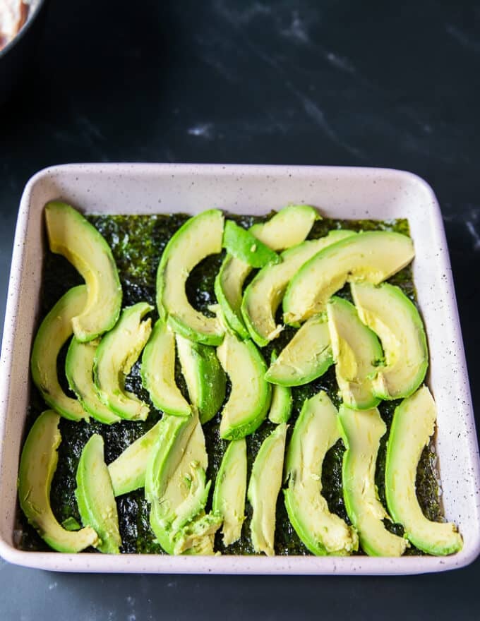 Avocado slices are arranged on top of the seaweed sheet in the baking pan