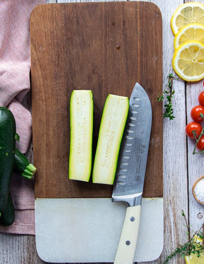 A zucchini cut in half on a wooden board using a sharp knife