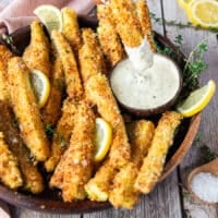 A hand dipping one zucchini fries into a garlic parmesan sauce