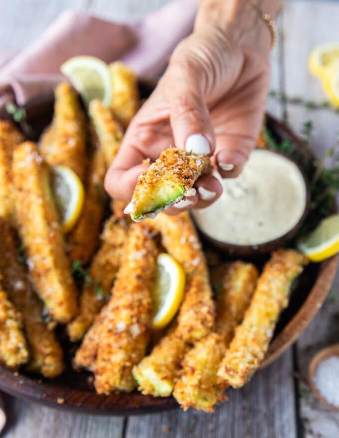 A hand holding a bitten air fryer zucchini fries showing the crunch coated and perfectly cooked zucchini 