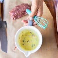 A hand holding the bowl of ready to pour vinaigrette over the carpaccio