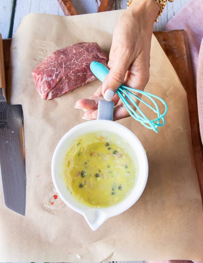A hand holding the bowl of ready to pour vinaigrette over the carpaccio 